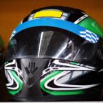 Trois casques intégraux de karting noirs avec designs verts, bleus et jaunes, posés côte à côte