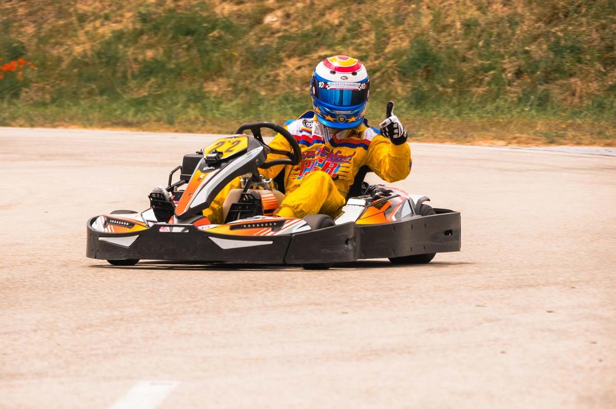 Pilote en combinaison jaune et noire conduisant un kart sur piste asphaltée en plein jour