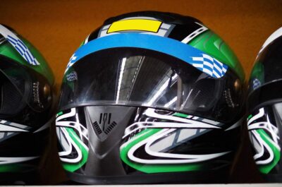 Trois casques intégraux de karting noirs avec designs verts, bleus et jaunes, posés côte à côte