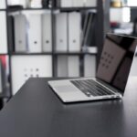 Un ordinateur portable ouvert sur un bureau, étagères rangées derrière