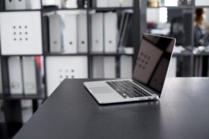 Un ordinateur portable ouvert sur un bureau, étagères rangées derrière