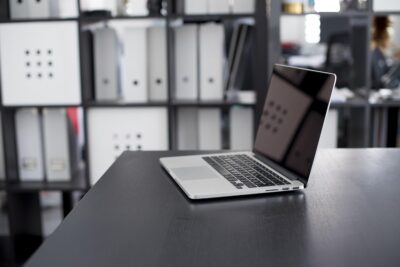 Un ordinateur portable ouvert sur un bureau, étagères rangées derrière