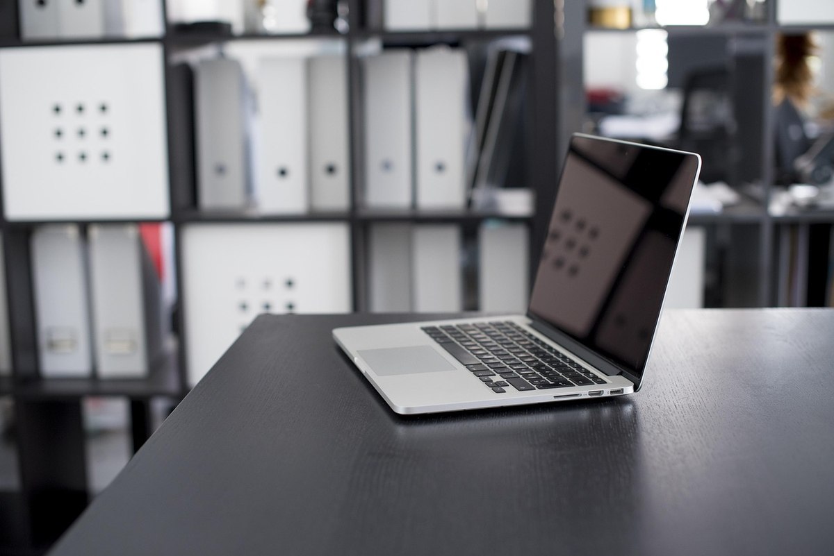 Un ordinateur portable ouvert sur un bureau, étagères rangées derrière