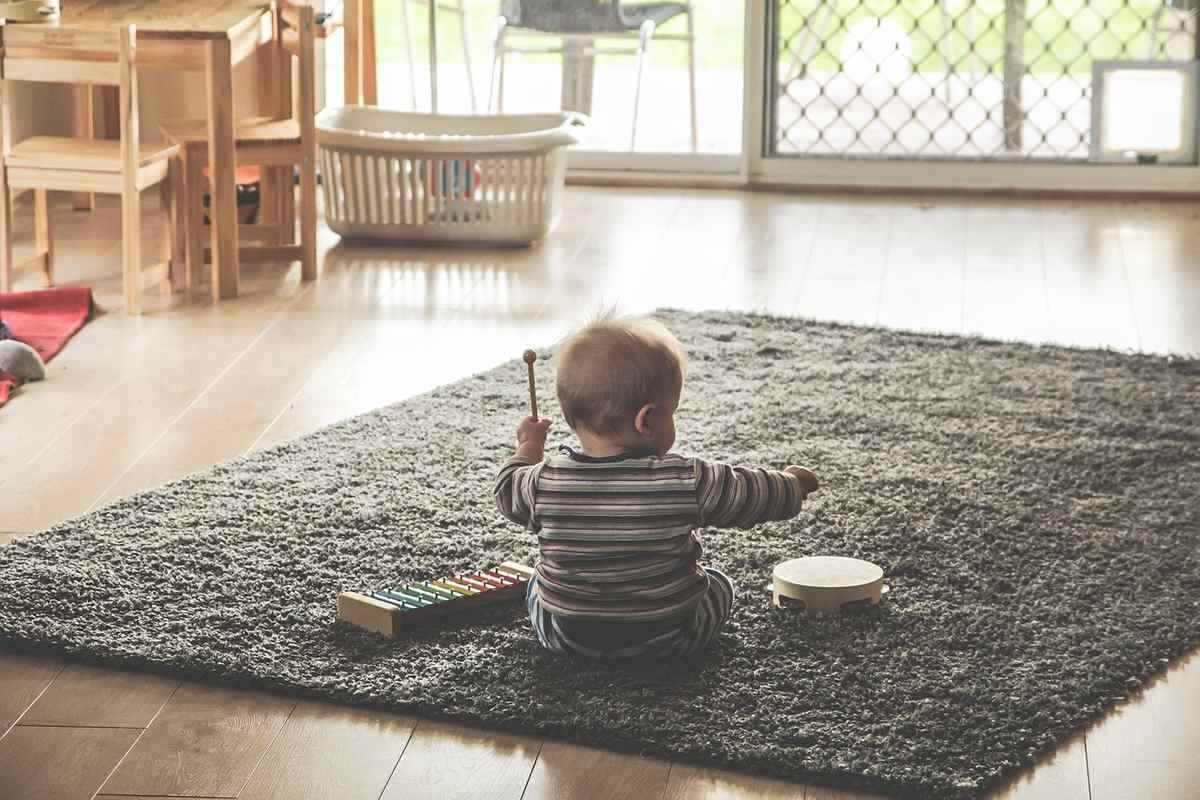 Nourrisson en striped shirt assis sur tapis gris à l'intérieur, tenant un bâton de musique