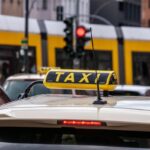 Taxi jaune avec panneau 'TAXI' sur toit, tram jaune à l'arrière-plan