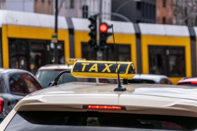 Taxi jaune avec panneau 'TAXI' sur toit, tram jaune à l'arrière-plan