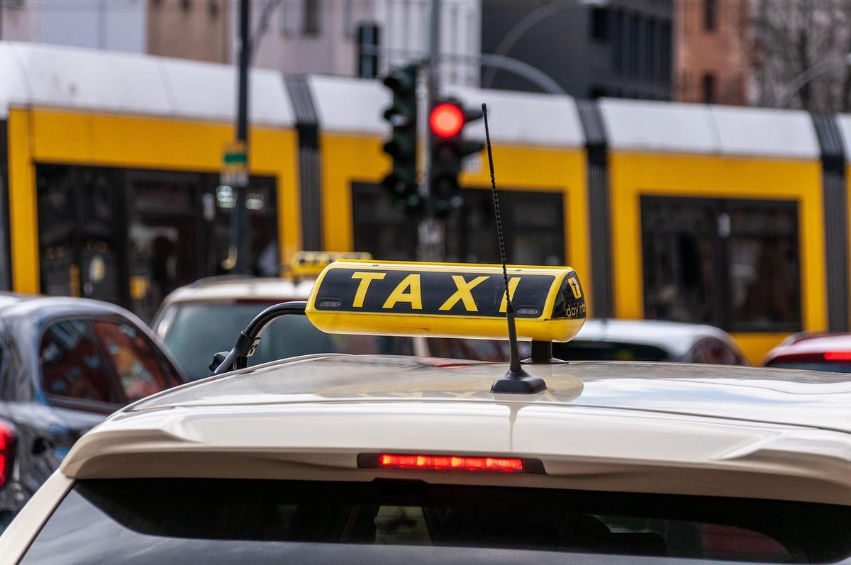 Taxi jaune avec panneau 'TAXI' sur toit, tram jaune à l'arrière-plan